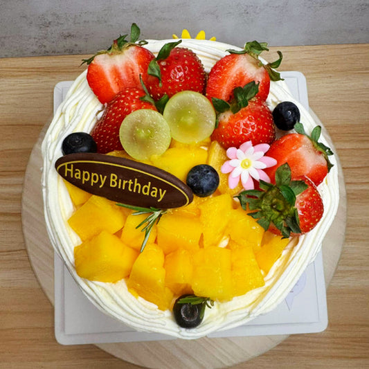 Fruit-topped birthday cake with 'Happy Birthday' sign on a wooden table.