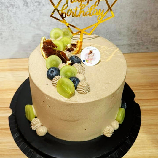 Beige cake with fruit toppings on a wooden surface, featuring a 'Happy Birthday' decoration.