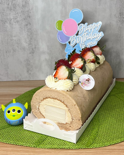 Birthday cake roll with strawberries and a 'Happy Birthday' topper on a green mat.