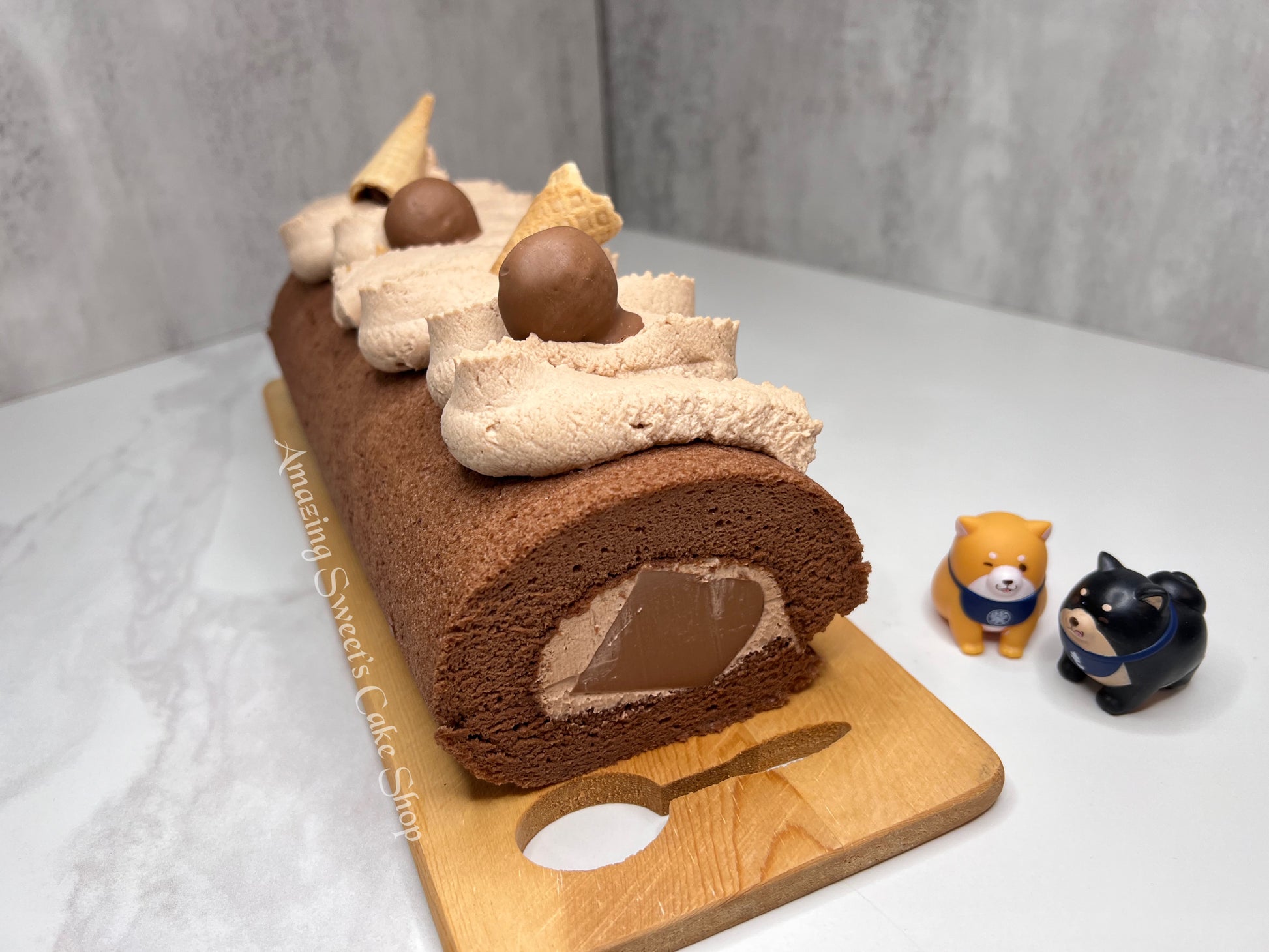 Chocolate swiss roll cake with decorative elements on a wooden board, small dog figurines in the background.