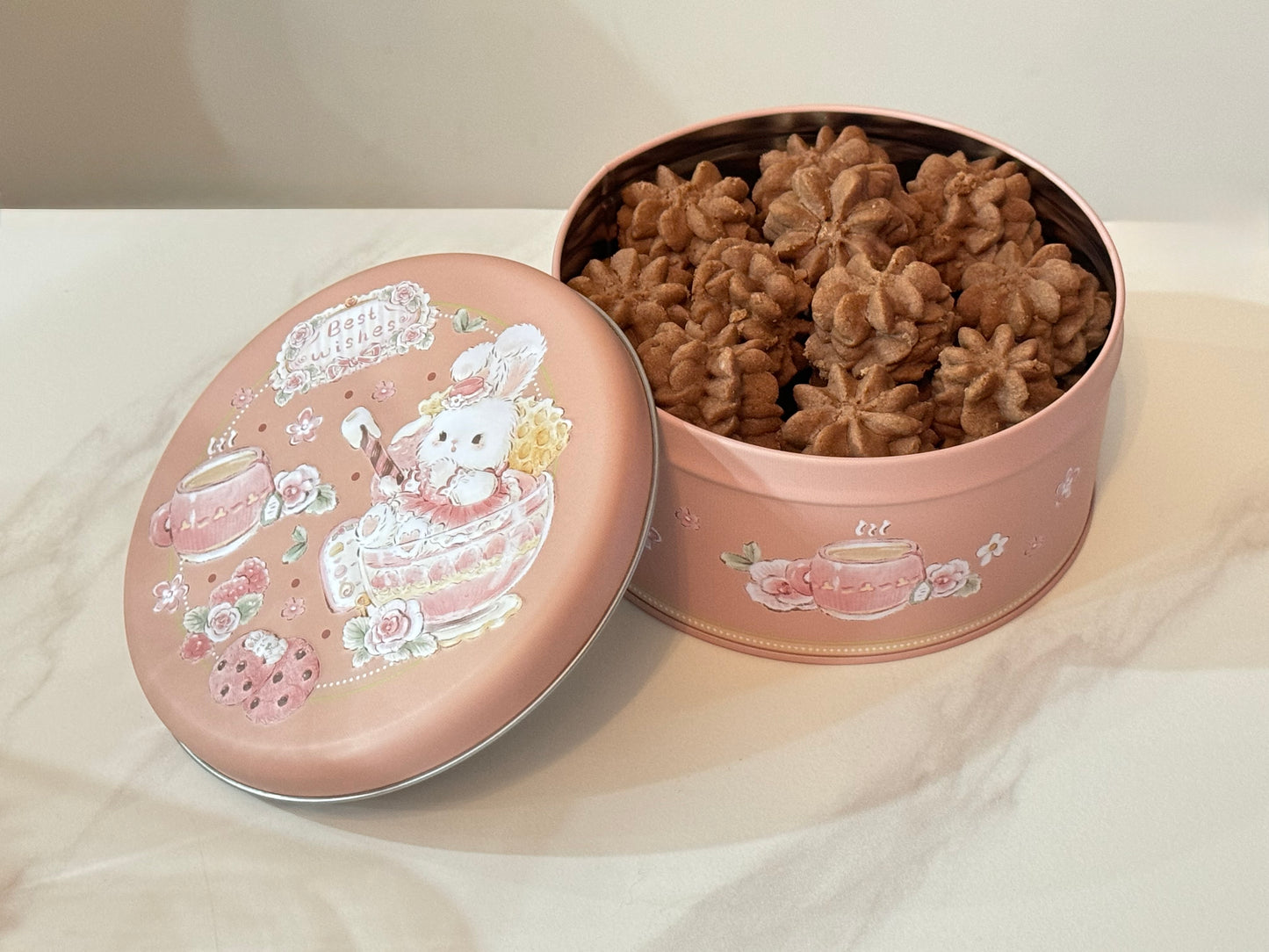 Decorative tin with a cartoon character lid containing brown cookies on a white surface.